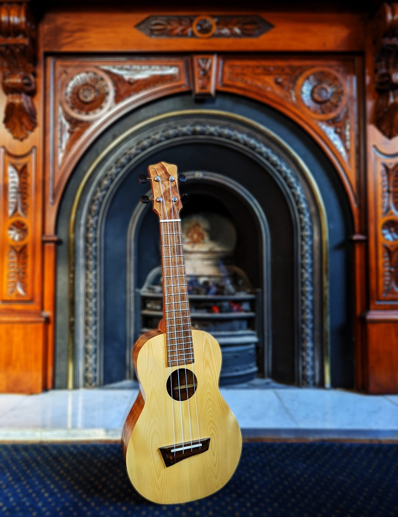 The Callitris ukulele standing in front of a Victorian fireplace