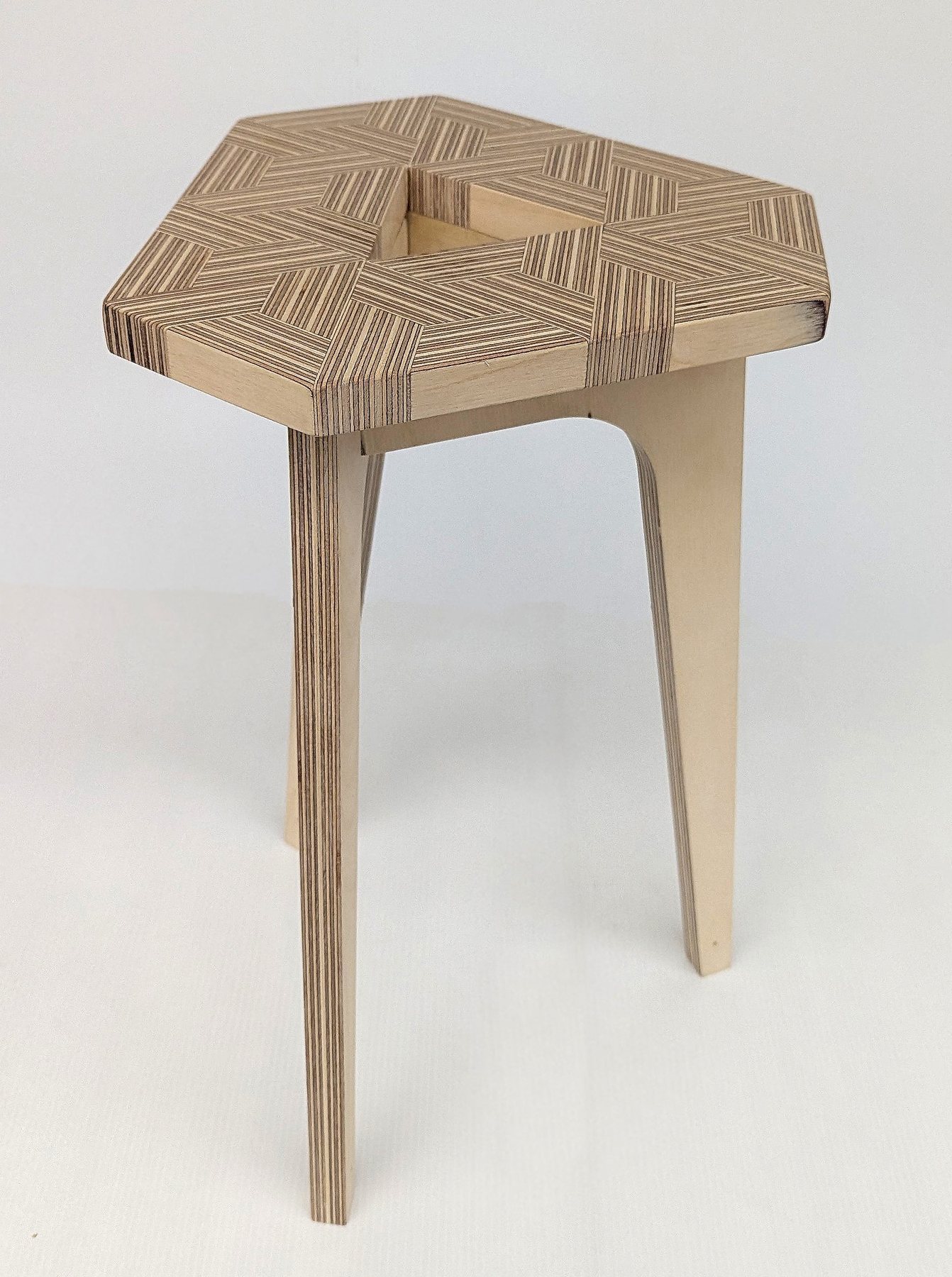Completed plywood stool: a hexagonal seat with a geometric end-grain pattern around a central void, on three splayed legs